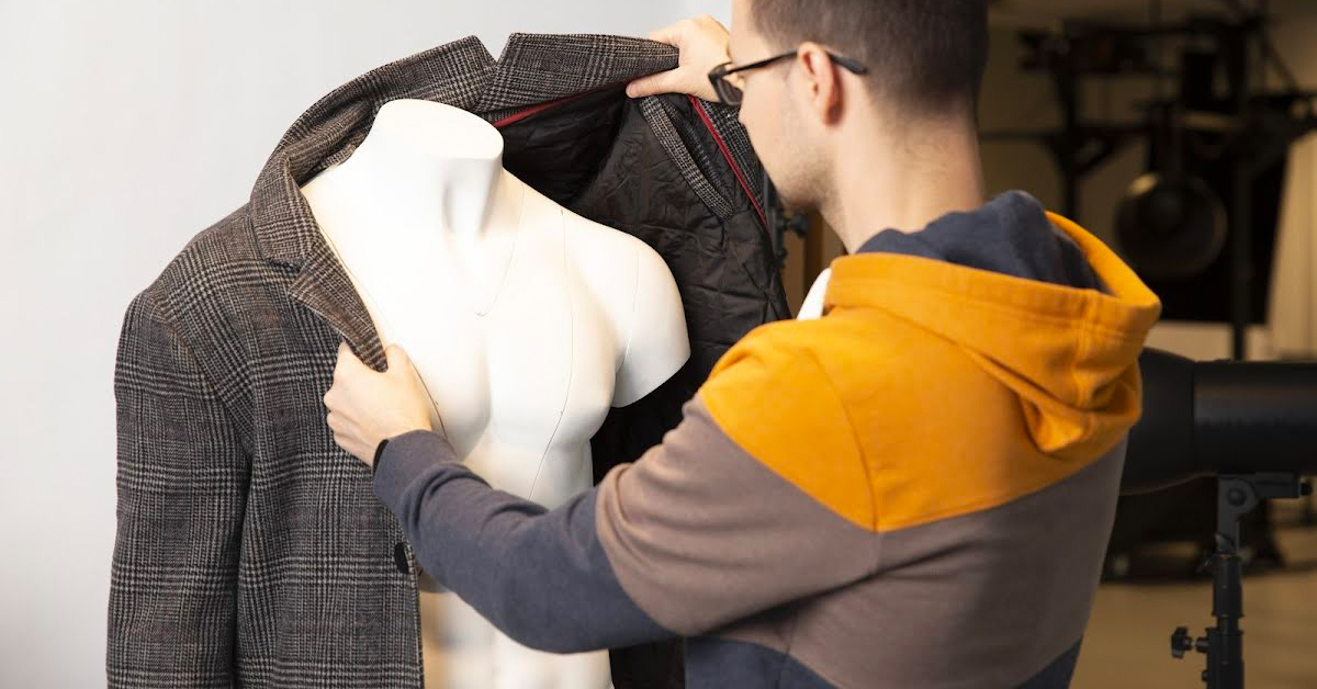 Photographer pulling sleeves of coat onto mannequin.