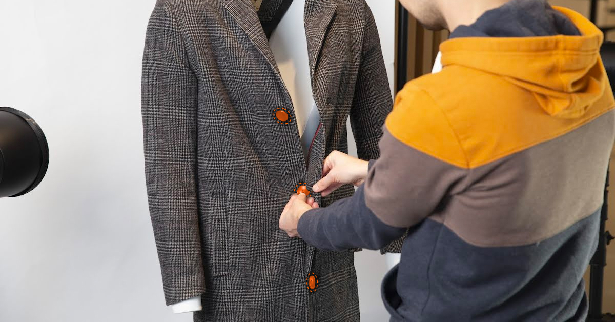 Photographer buttoning up coat on mannequin.