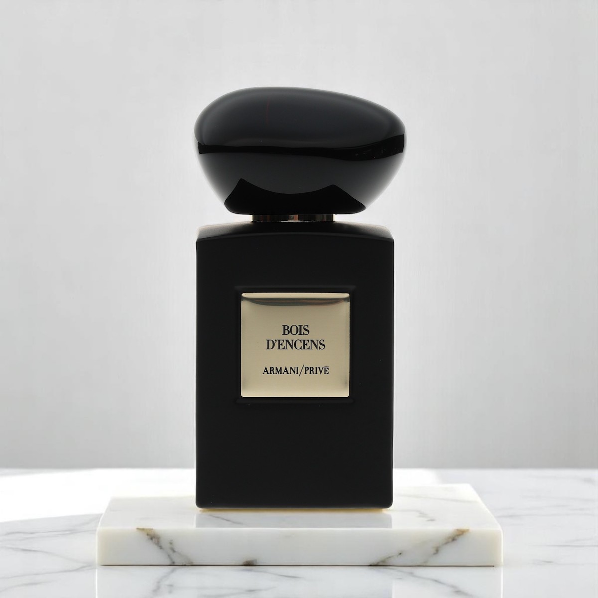 Bois D’Encens by Armani/Prive in a black and gold bottle sits atop marble on a matching background.